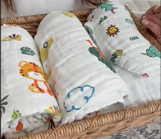 Load video: Baby wrapped in a soft muslin swaddle blanket from a 4-pack set, designed for naps, cuddles, stroller rides, and everyday comfort.